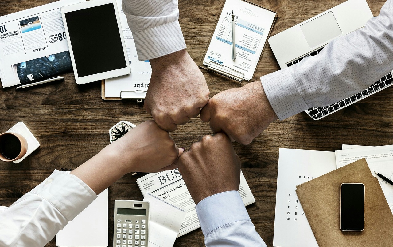 Mehrere Personen im Büro geben sich einen Fistbump als Zeichen der Zusammenarbeit und des Erfolgs.